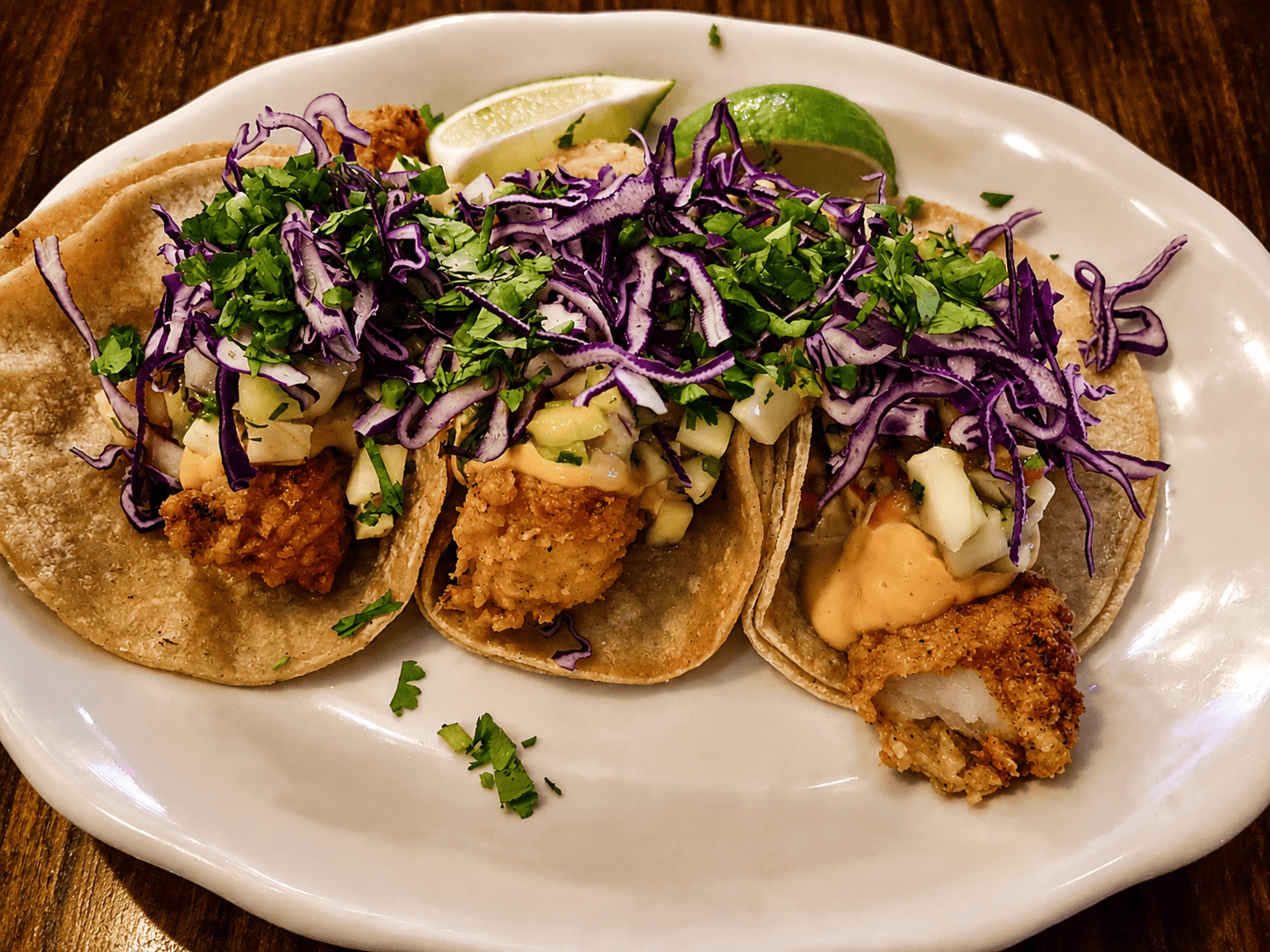 Three crispy fried fish tacos served on corn tortillas with shredded purple cabbage, fresh cilantro, lime, and chipotle mayo sauce