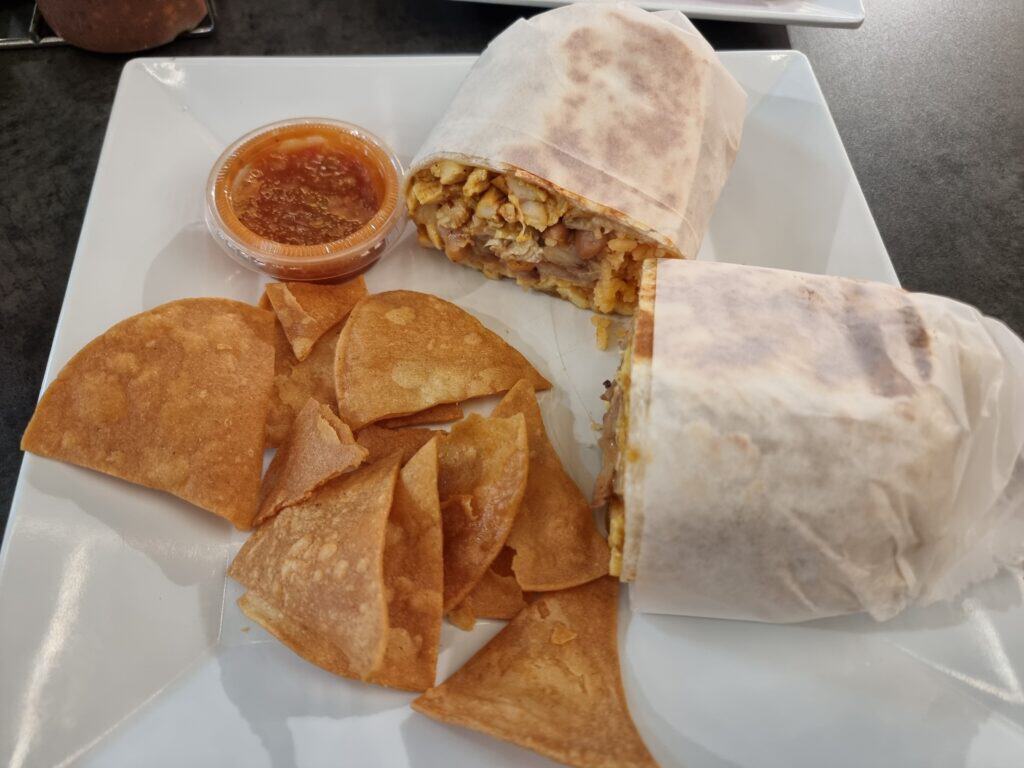 A large chicken burrito sliced in half revealing rice and bean filling, served on a square plate with crispy tortilla chips and salsa.