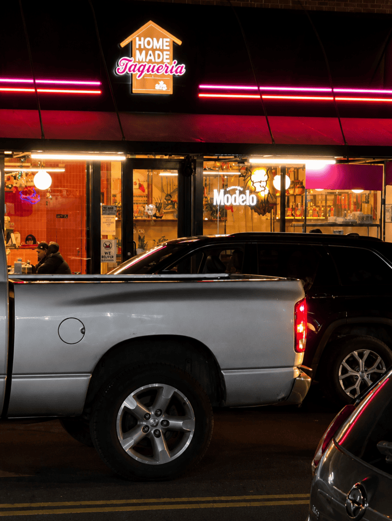Neon pink and white illuminated storefront sign for Homemade Taqueria at night on Roosevelt Avenue in Jackson Heights.