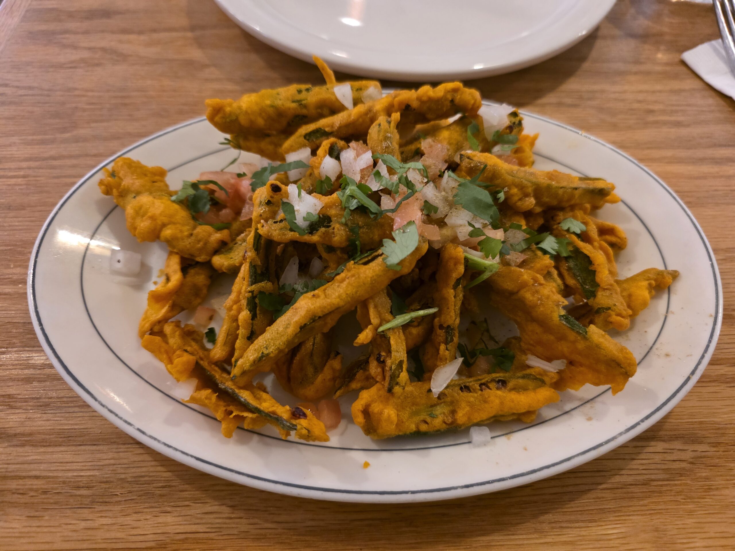 A plate of crispy golden-brown fried okra seasoned with fresh cilantro, diced raw onions, and chopped tomatoes.