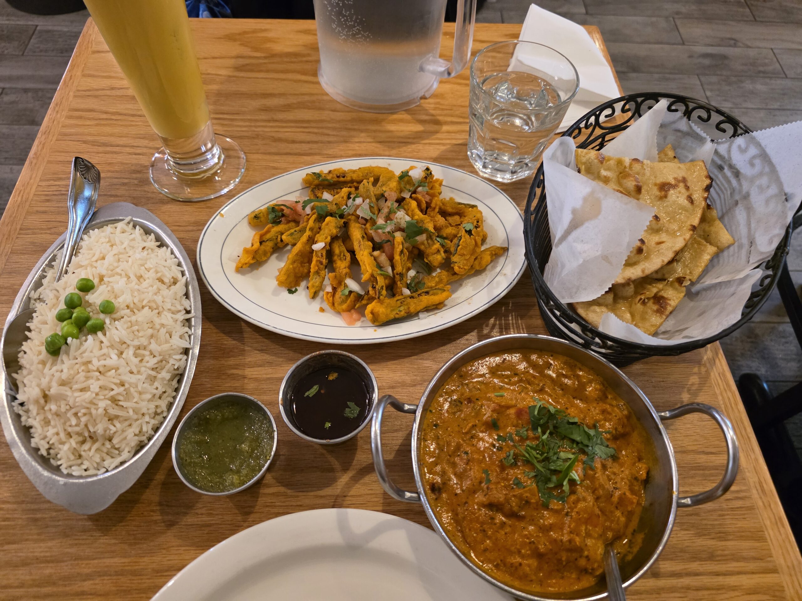 A top-down view of a full Indian dinner spread at Jackson Diner including chicken tikka masala, rice, fried okra, mango lassi, and fresh naan.