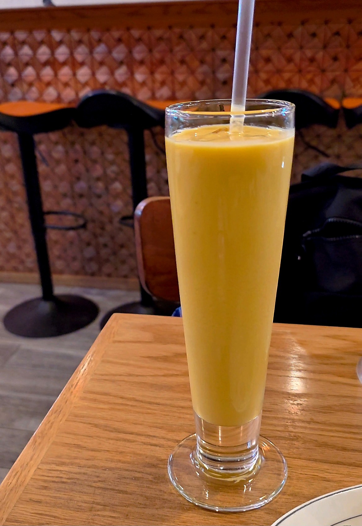 An eye-level view of an active dining table at Jackson Diner featuring a tall glass of bright yellow mango lassi next to bowls of chicken curry and appetizers.