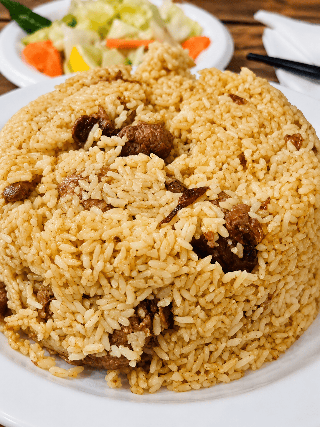 A classic serving of chicken biryani with spiced basmati rice and tender pieces of marinated chicken on a white plate.