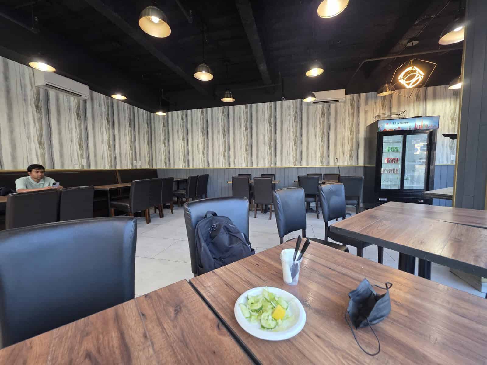The clean, modern dining area at Khalil Biryani House in Jackson Heights, featuring dark leather chairs, wooden tables, textured wallpaper, and hanging light fixtures.