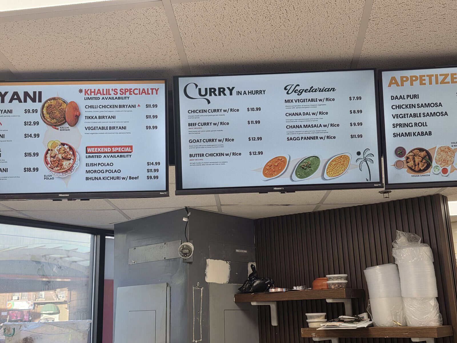 Digital menu boards at Khalil Biryani House displaying prices for Biryani, Curry in a Hurry, vegetarian options, and appetizers