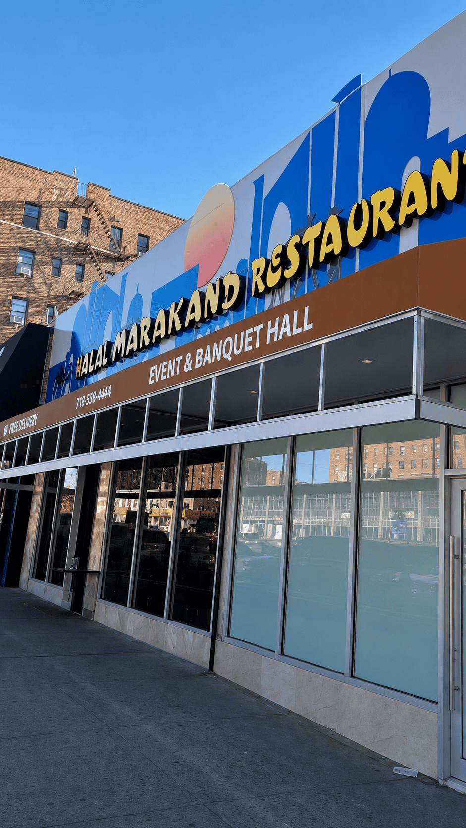 The wide exterior storefront of Halal Marakand Restaurant and Event Banquet Hall under a clear blue sky in Rego Park, Queens.