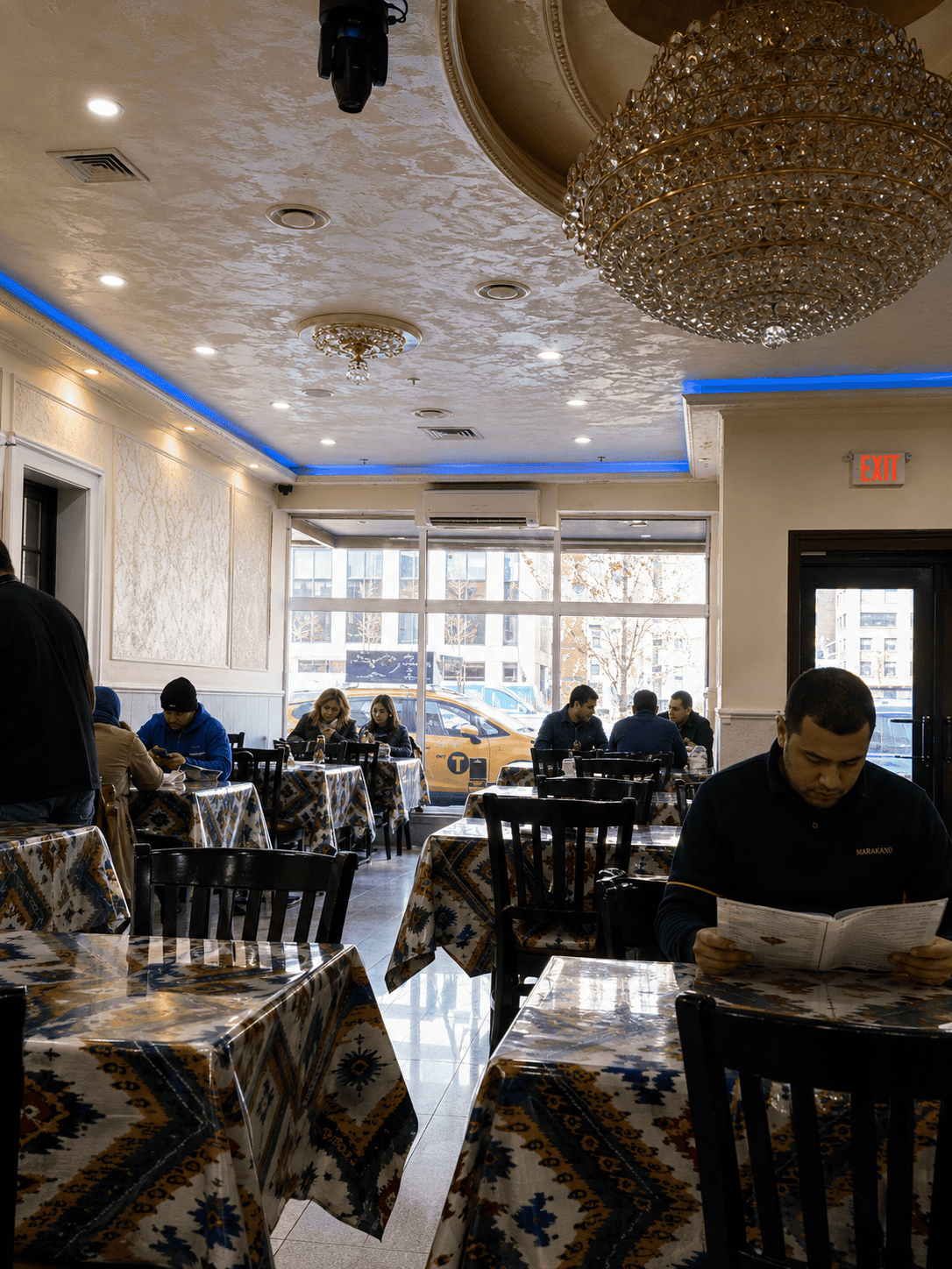  Inside the dining room of Marakand Uzbek restaurant featuring patterned traditional tablecloths, ornate crystal chandeliers, and patrons reading menus.