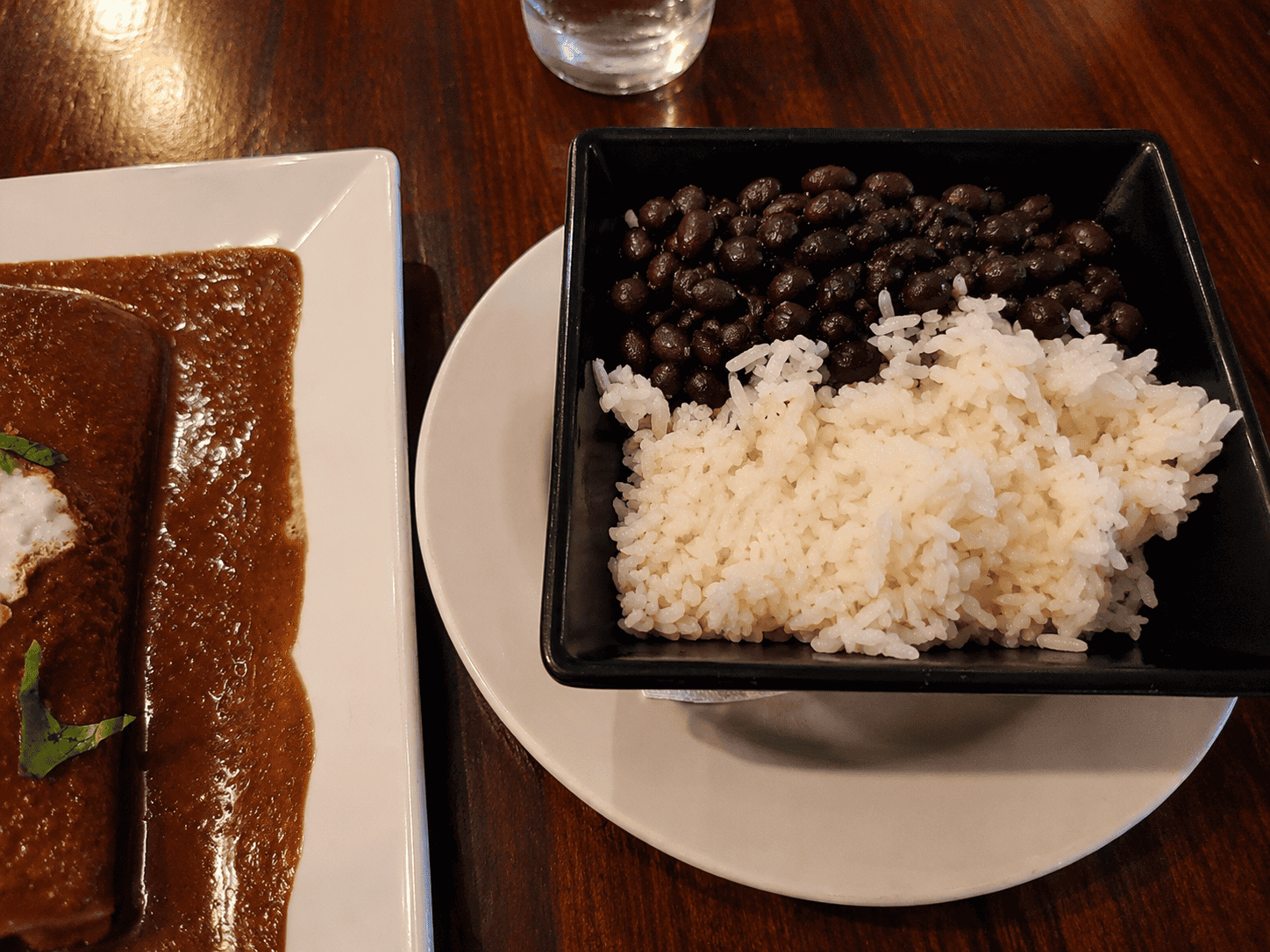 A side dish bowl of white rice and seasoned black beans served alongside enchiladas at Laly's Restaurant