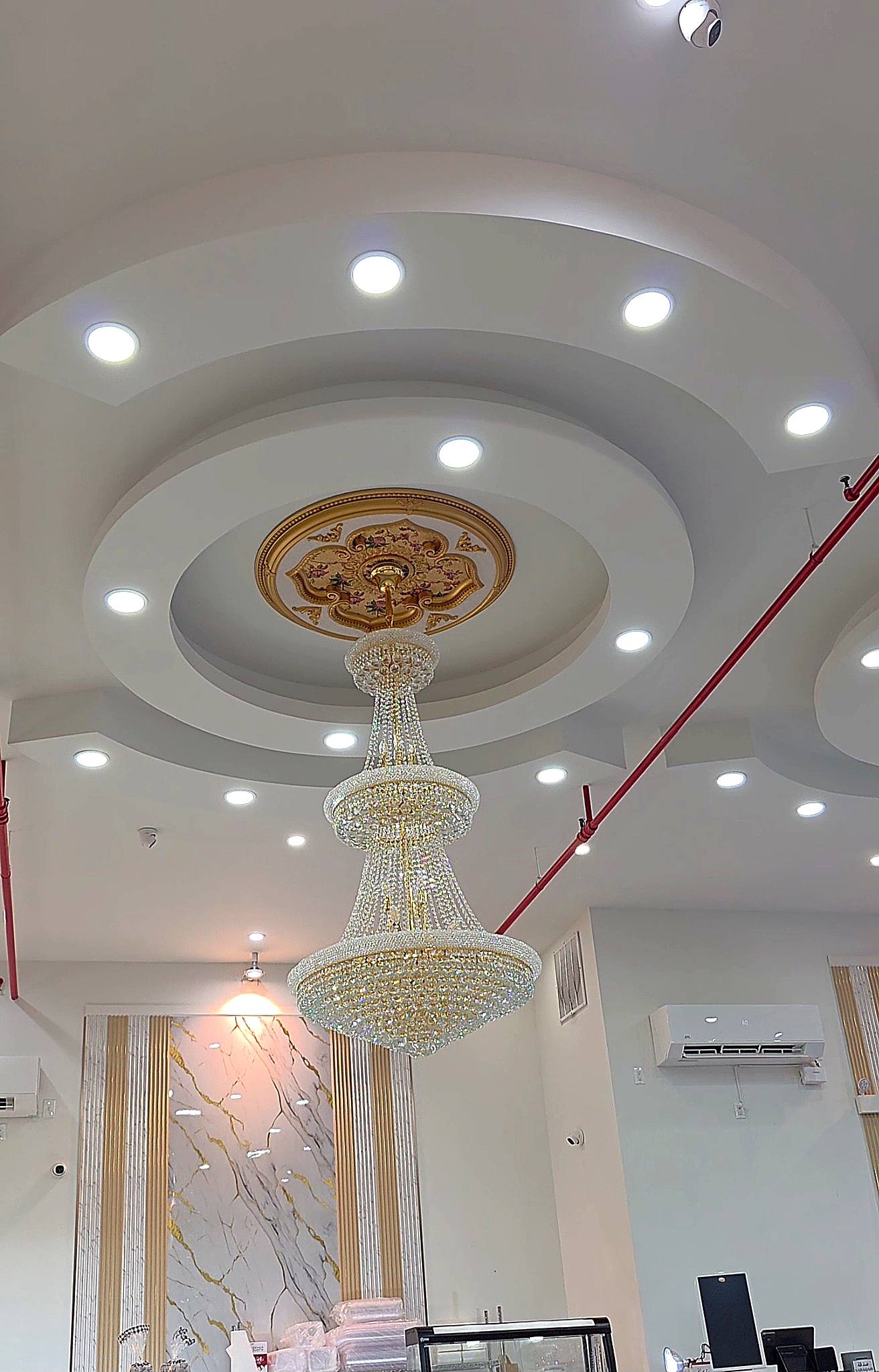 Elegant, large tiered crystal chandelier hanging from a recessed circular ceiling inside Shanai Party Hall.