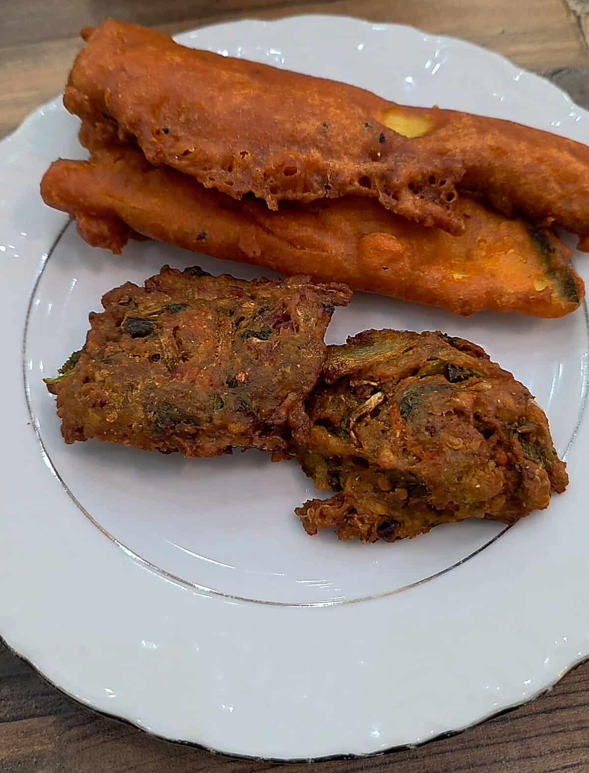 Crispy, deep-fried golden brown onion fritters and elongated fried eggplant pakoras served fresh on a white plate.