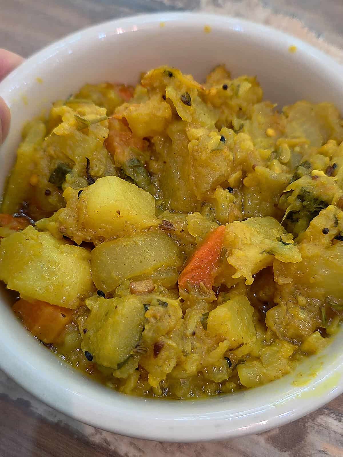 A close-up bowl of thick, spiced mixed vegetable curry featuring potatoes, carrots, and traditional South Asian spices.