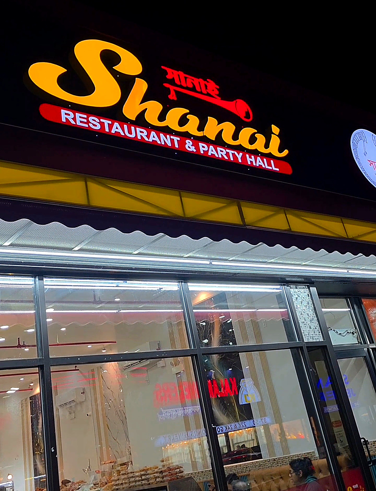 The vibrant red and yellow exterior neon sign of Shanai Restaurant & Party Hall at night in Jackson Heights, Queens.