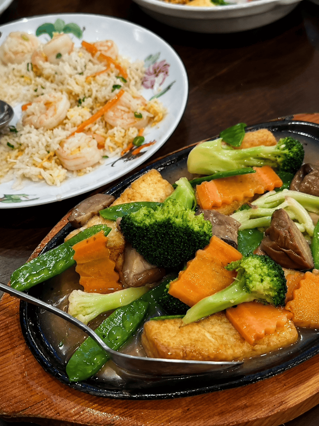 A sizzling hot platter filled with fried tofu blocks, broccoli, carrots, and snow peas in a savory brown sauce.