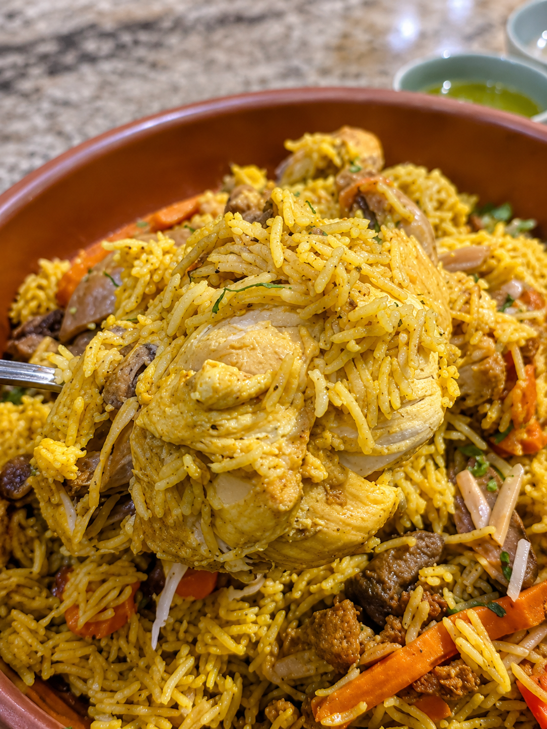 A detailed close-up shot of the chicken Maqlouba, highlighting the large piece of tender chicken mixed with rice and vegetables.