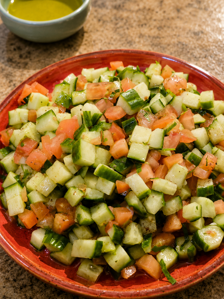 A close-up view of a vibrant Palestinian salad made with finely diced tomatoes and cucumbers in a red ceramic bowl.