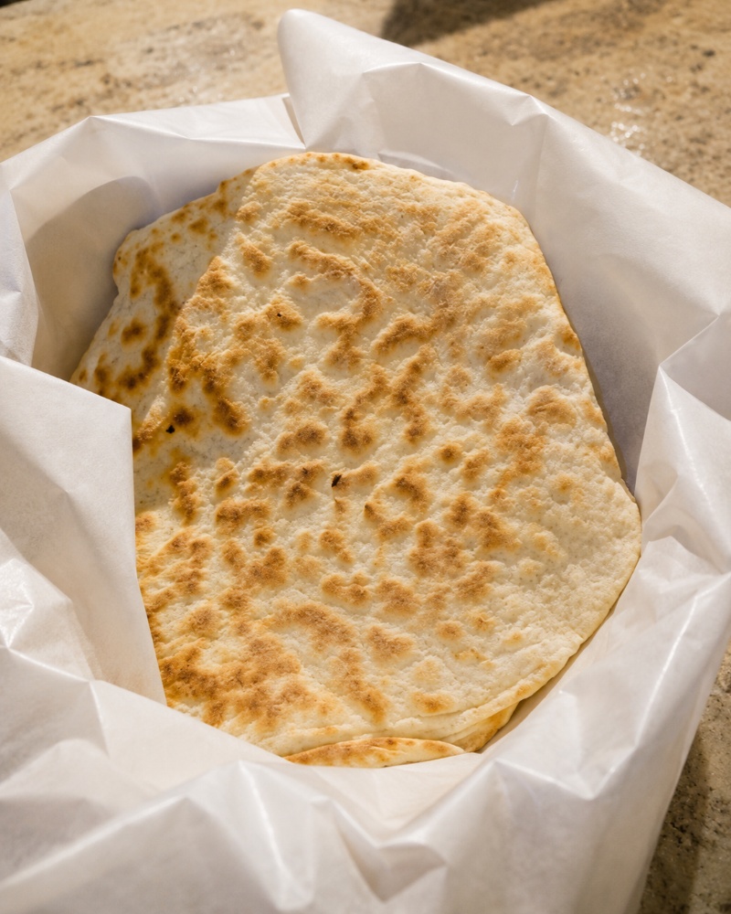 A basket filled with warm, fresh khubz (Palestinian pita bread) lined with white paper.