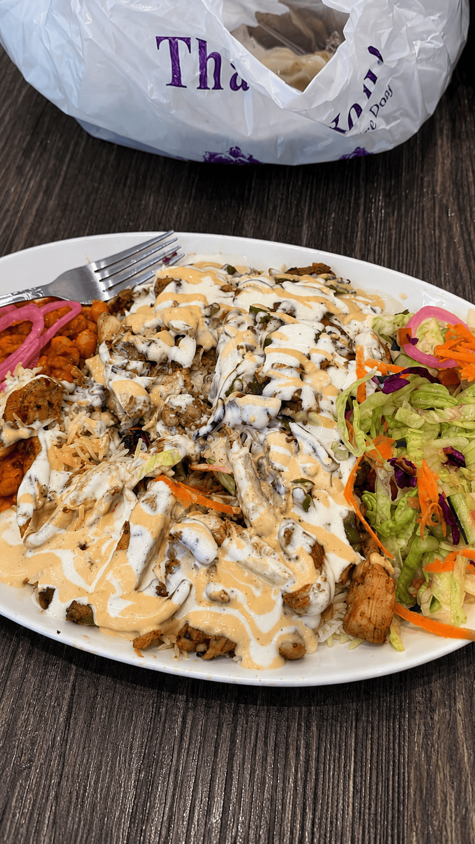 A massive chicken shawarma rice platter completely covered in a criss-cross pattern of white sauce and orange hot sauce, served with a side of chopped lettuce salad and pickled onions.
