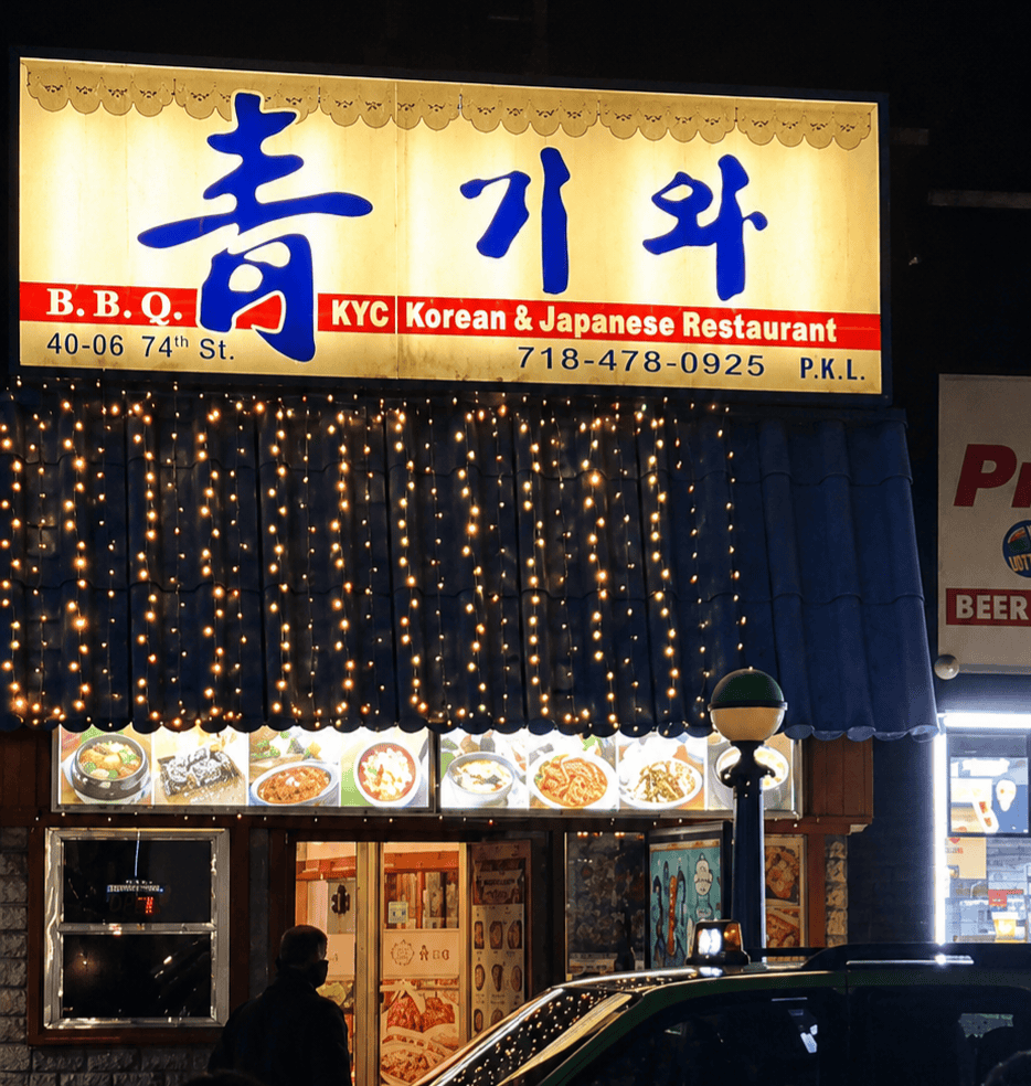 Illuminated restaurant storefront sign for Chung Ki Wa at night reading BBQ KYC Korean and Japanese Restaurant with warm fairy lights under the awning.