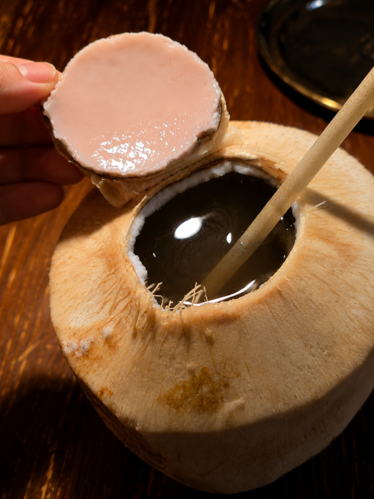 A fresh young coconut opened up with a straw served as a refreshing drink at a restaurant table
