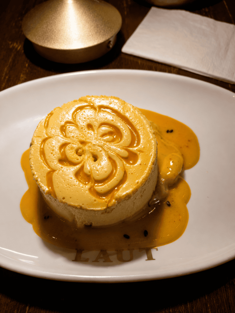 A velvety mango cheesecake drizzled with tropical fruit puree and black sesame seeds on a white plate