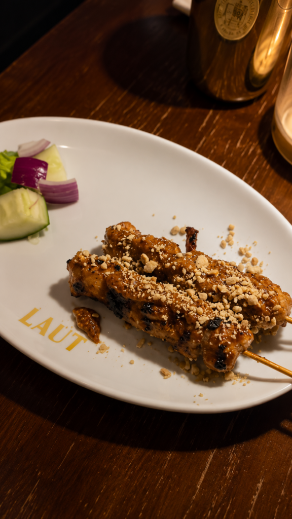 Grilled chicken satay skewers topped with crushed peanuts on a white plate branded with the Laut logo