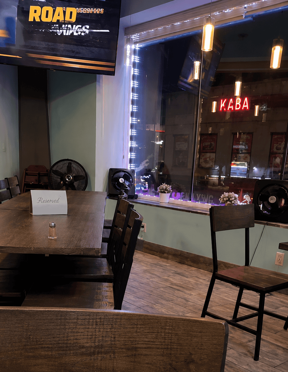 The casual second-floor dining area of Moonlite Grill and Chicken at night, featuring large glass windows overlooking Broadway with green LED accent lighting.