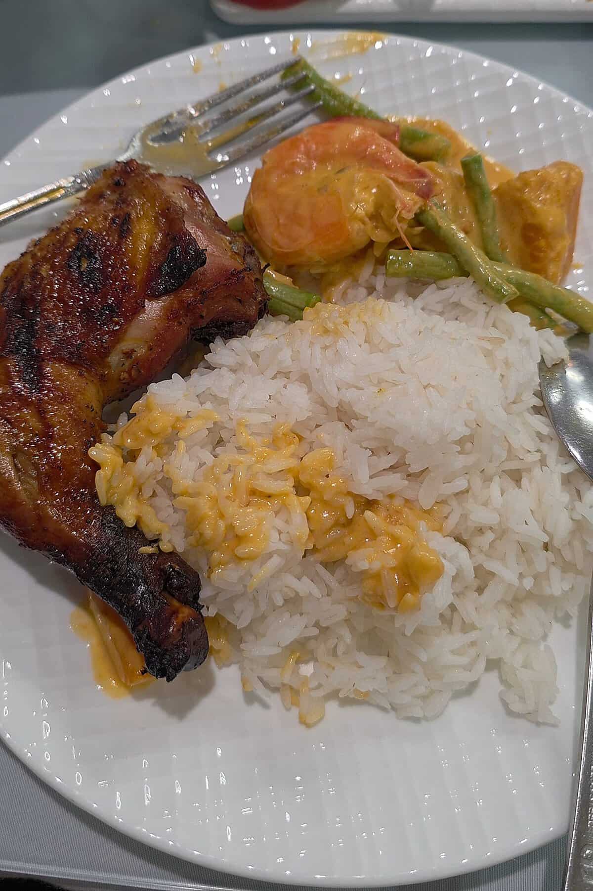 
A dinner plate featuring a portion of grilled chicken inasal and creamy ginataang kalabasa vegetable stew served alongside a mound of white rice.

