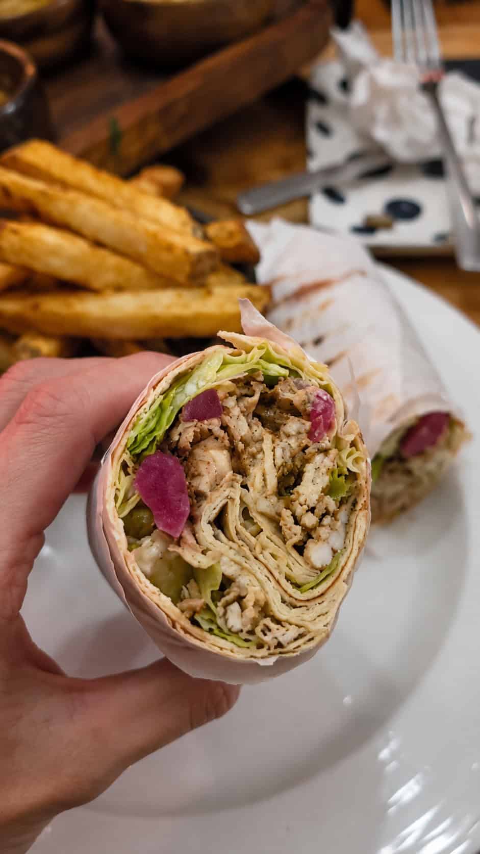Hand holding a cross-section of a chicken shawarma wrap showing shredded chicken lettuce and pickled turnips