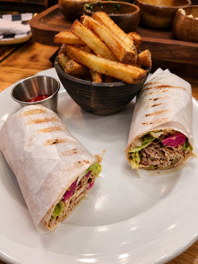 Halal chicken shawarma wrap cut in half served with a cup of thick cut french fries