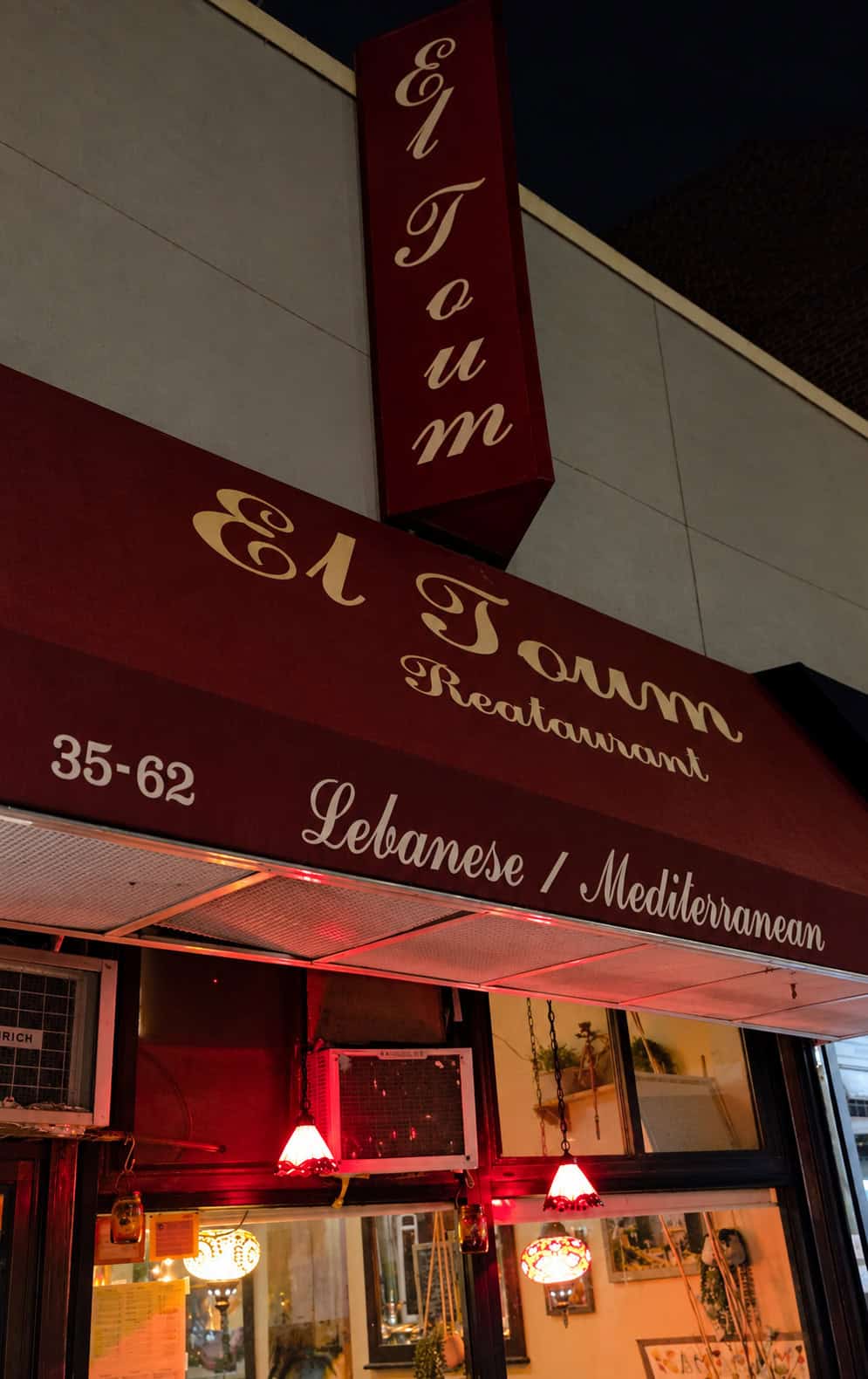 Red awning and vertical sign of El Toum Lebanese Mediterranean restaurant in Jackson Heights Queens