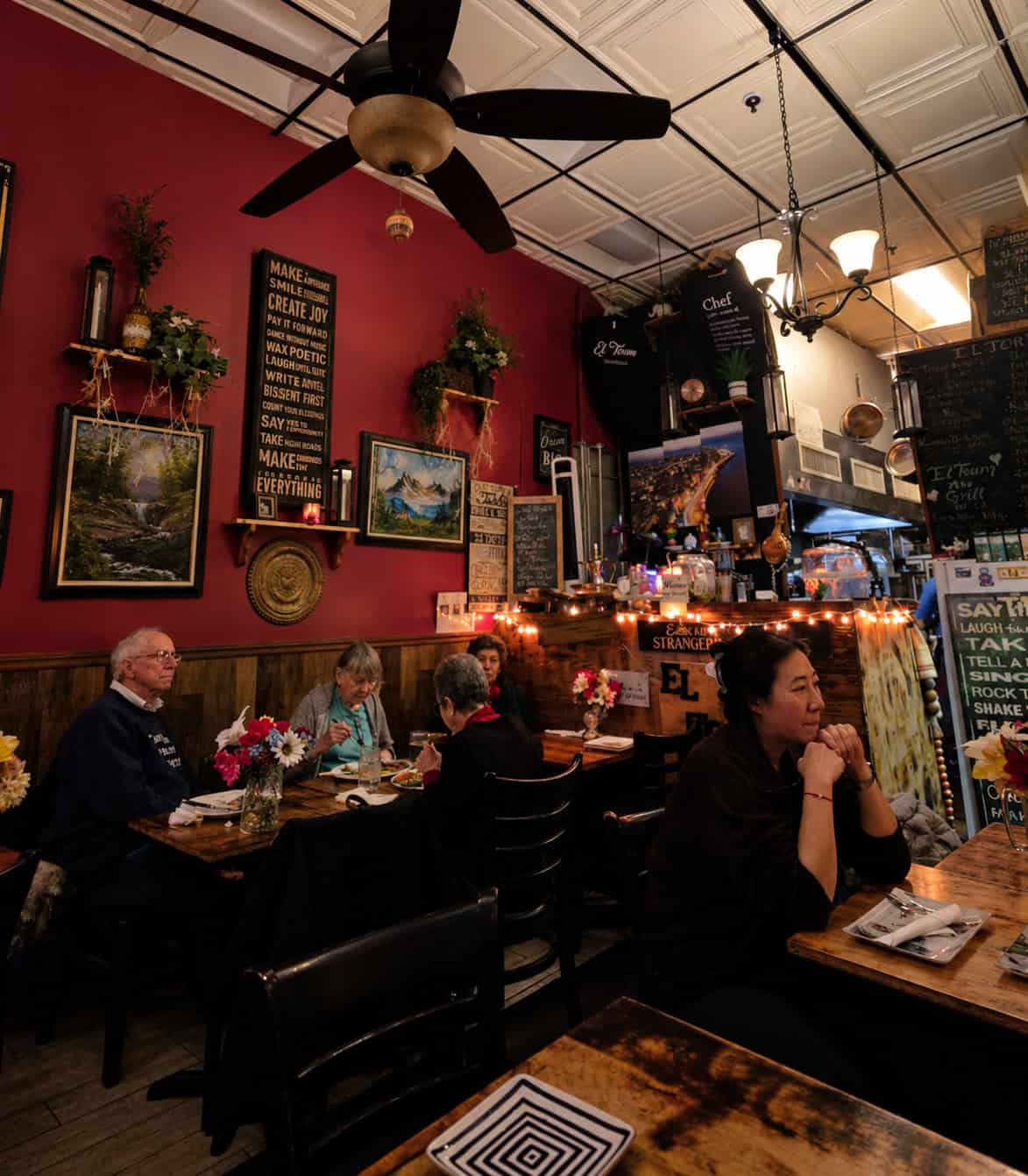 Cozy dining room interior at El Toum featuring deep red walls framed artwork and string lights