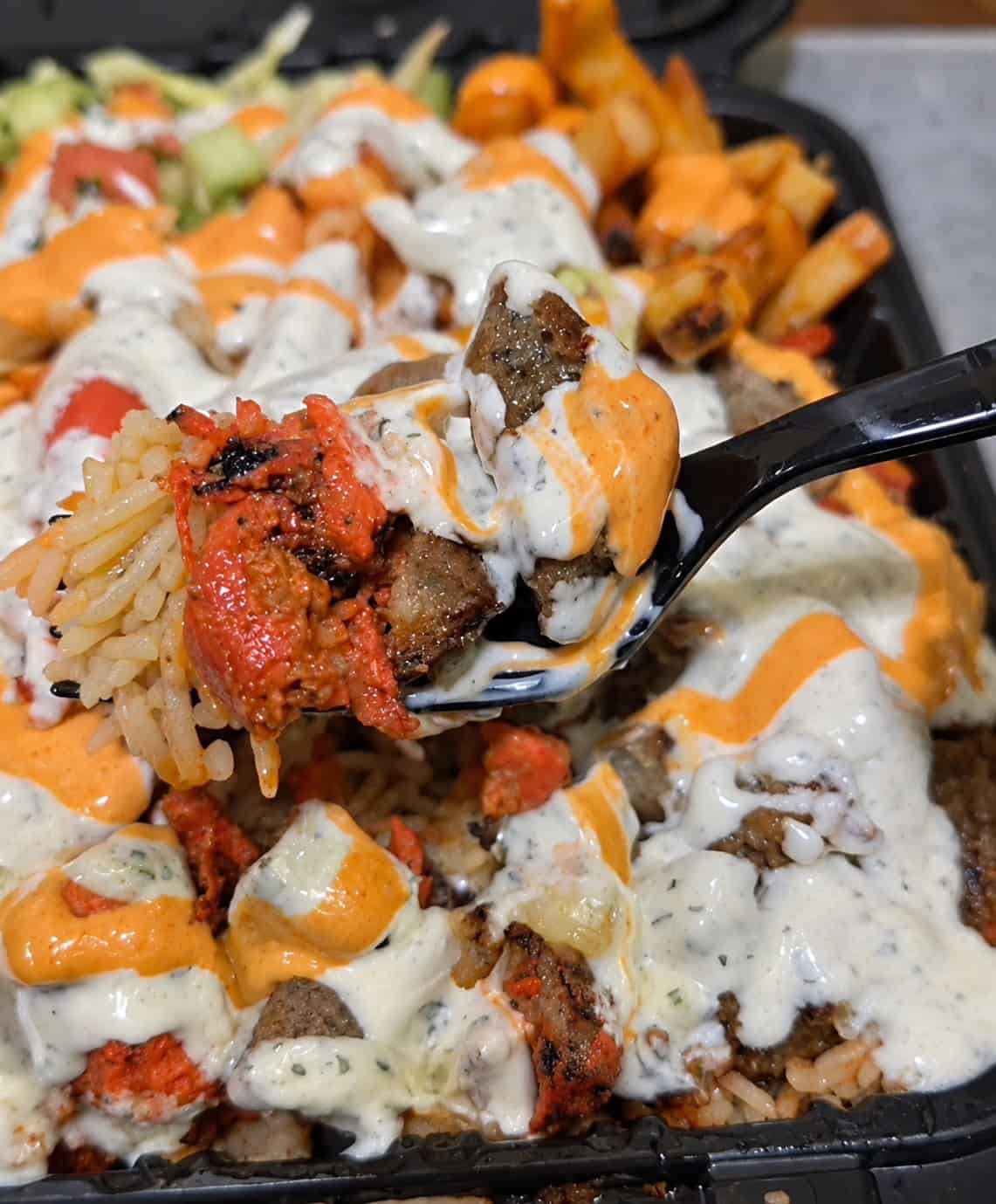 Fork holding a spoonful of spiced rice, chicken, lamb, white sauce, and hot sauce from Halal Eats platter
