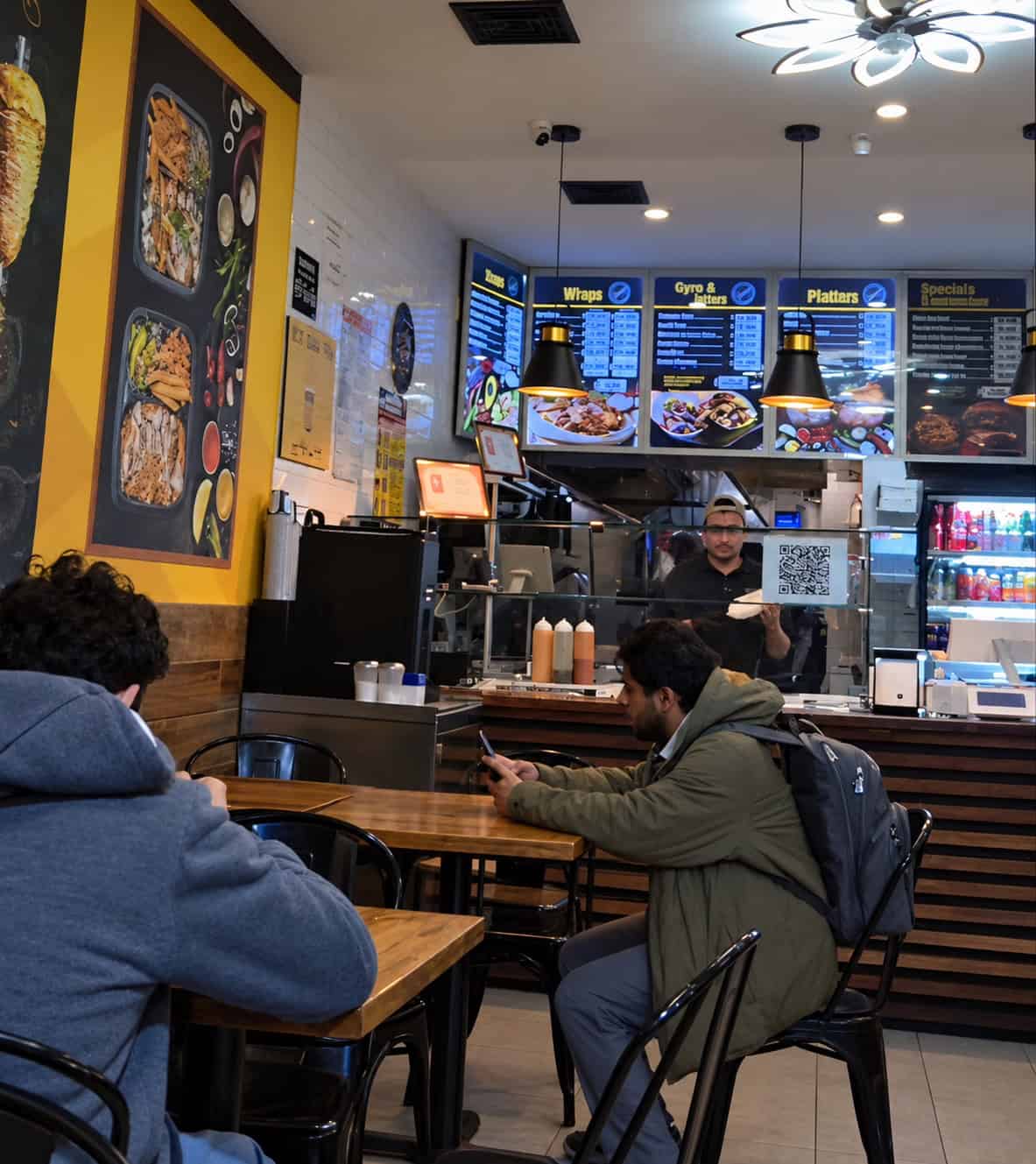 Small interior dining space at Halal Eats with wooden tables, black chairs, and digital menu boards