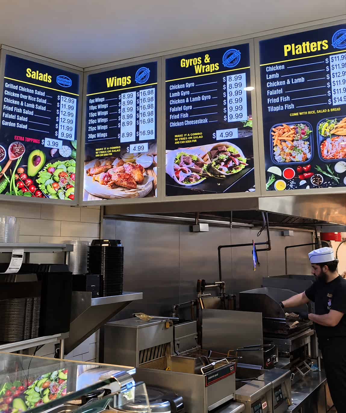 Digital menu board above order counter at Halal Eats displaying prices for platters, gyros, and wings
