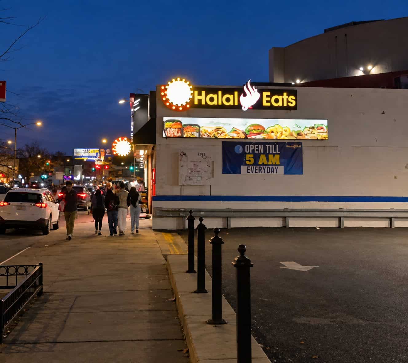 Exterior illuminated storefront of Halal Eats on Queens Boulevard in Elmhurst Queens featuring late night sign