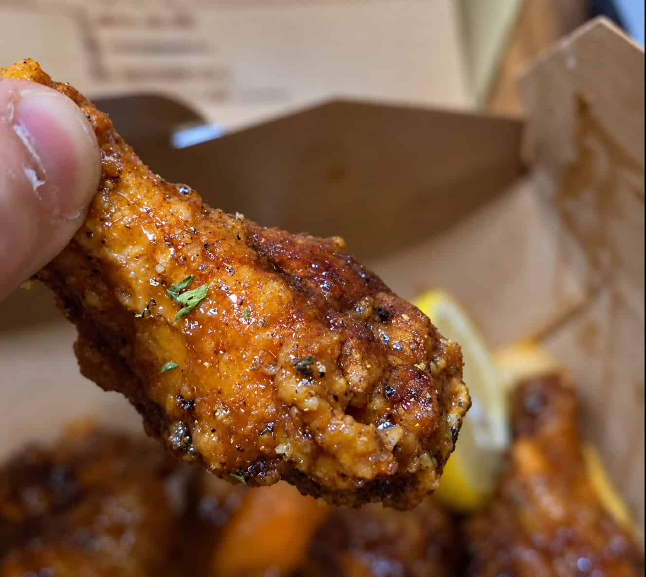 Hand holding a glazed honey garlic lemon pepper chicken wing showing seasoned crispy coating