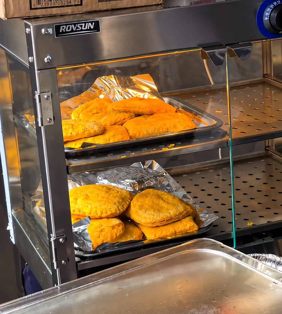Heated display case stocked with fresh golden Jamaican beef patties at Robinson Valley tent