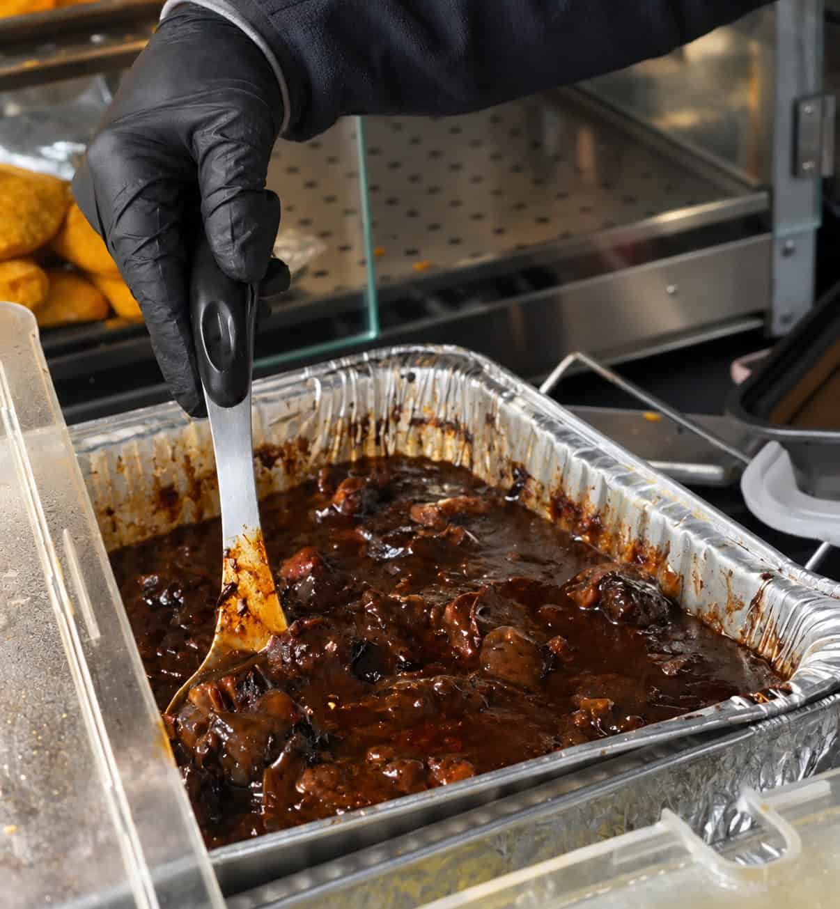 Large steam tray filled with slow-cooked Jamaican oxtail stew in rich dark gravy