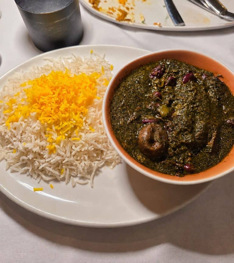 Bowl of dark green Ghormeh Sabzi herb stew served alongside white basmati rice