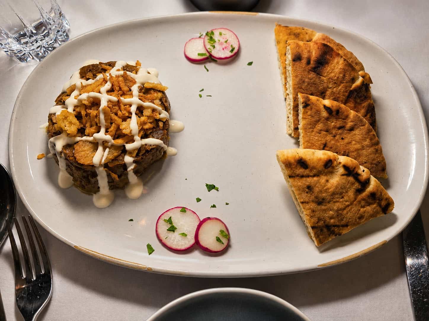 Bowl of warm Kashke Bademjoon Persian eggplant dip topped with crispy onions and pita bread