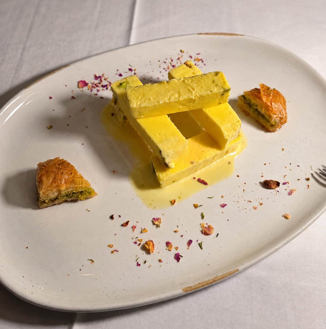 Scoops of yellow saffron ice cream served with layers of flaky nutty baklava