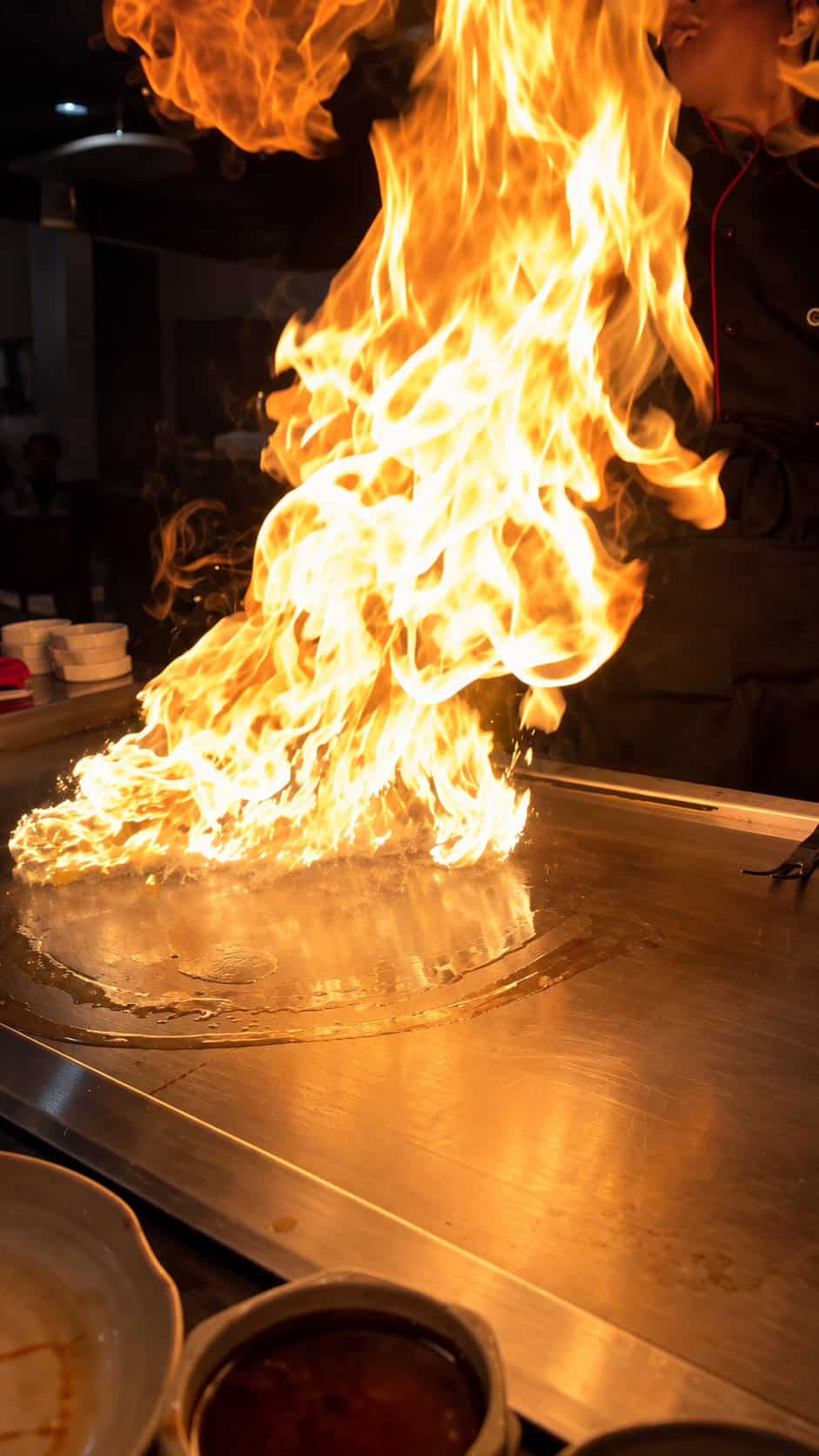 Chef igniting a large teppanyaki grill flame performance at the hibachi table