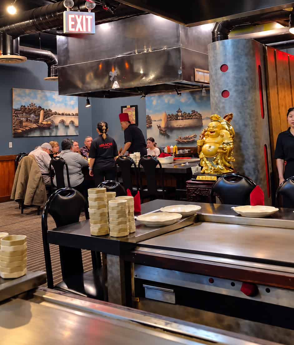 Interior view of Shogun Hibachi featuring teppanyaki grill tables, industrial ceiling, and traditional artwork