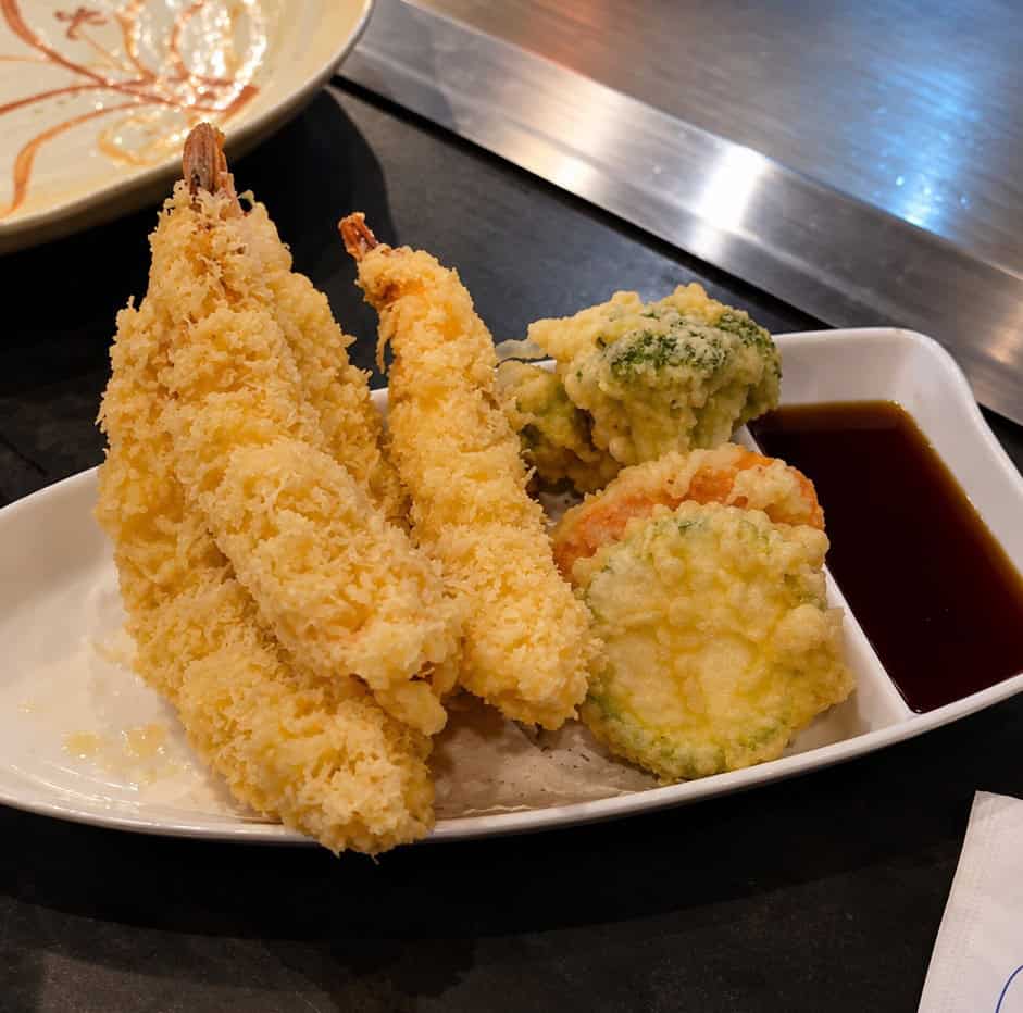 Crispy golden battered shrimp and fried vegetables arranged on a white serving plate with tempura dipping sauce