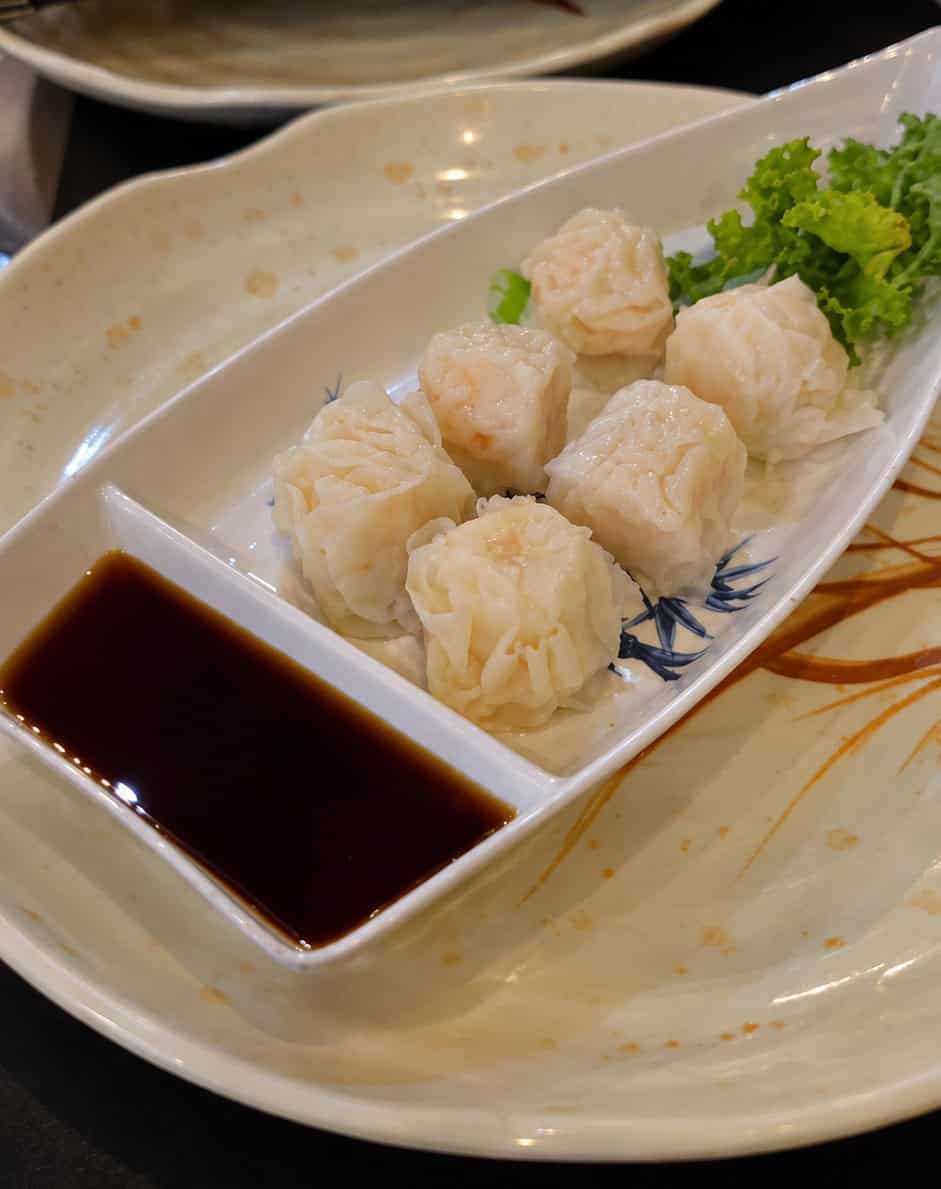 Six pieces of delicate steamed shrimp dumplings served in a rectangular ceramic dish with soy dipping sauce