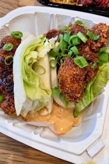 Two Crispy Chicken Buns in a white takeout container with soft steamed bao bread, crispy fried chicken, lettuce, and orange sauce
