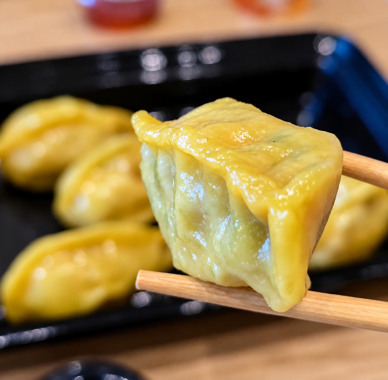 Close-up view of wooden chopsticks holding a juicy yellow-skinned Chicken and Cabbage Dumpling