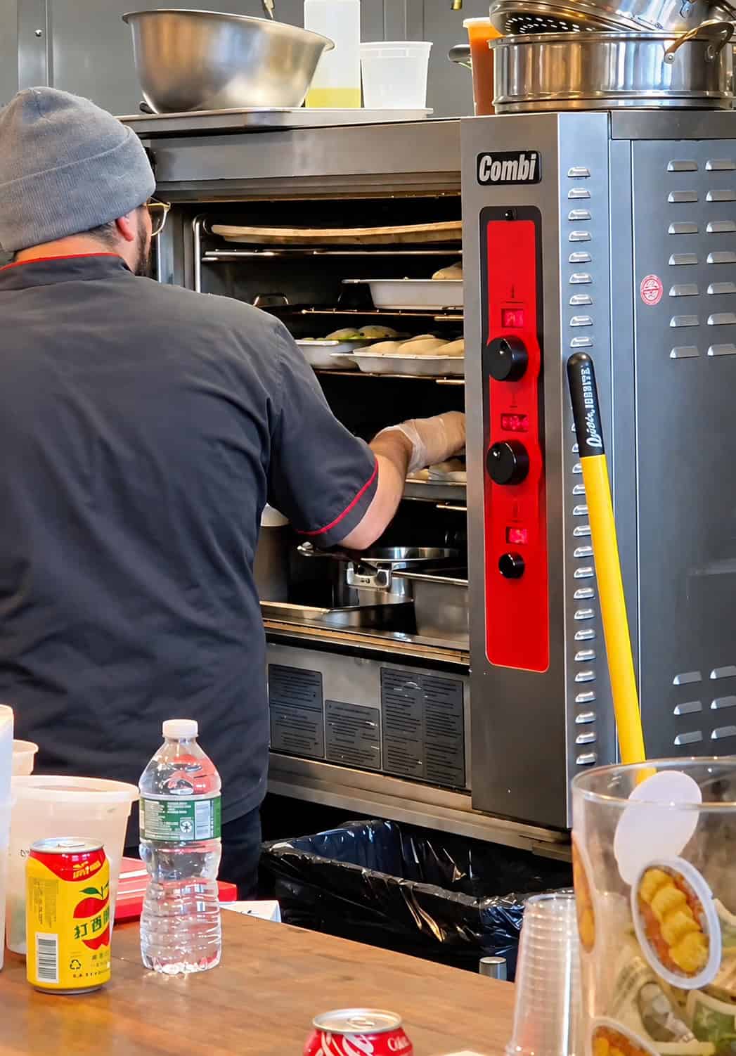 Kitchen staff member preparing dim sum in open kitchen at Nom Wah Pier 57 near commercial steamer equipment