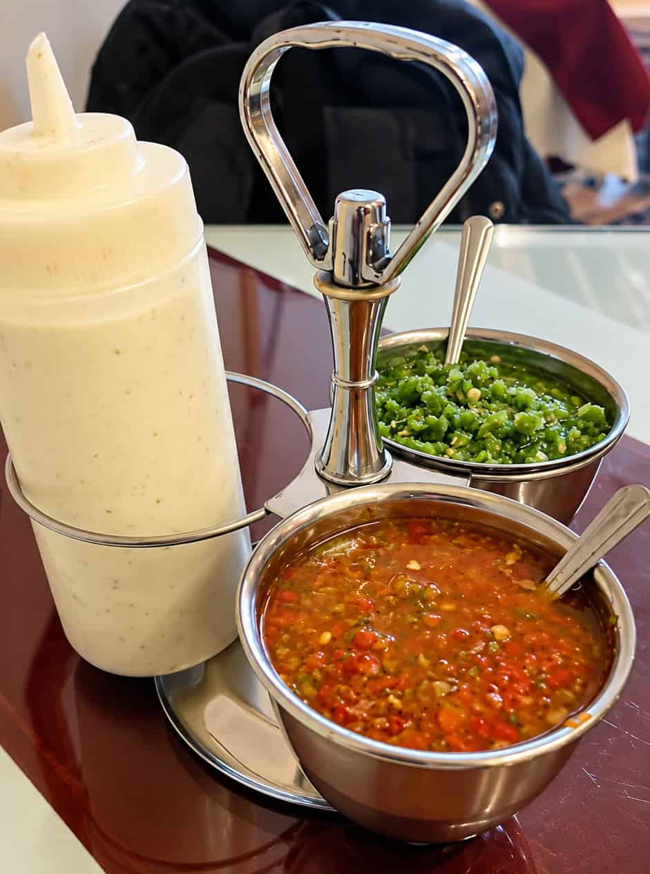 Table condiment caddy holding red spicy chutney, green herb chutney, and garlic yogurt squeeze bottle