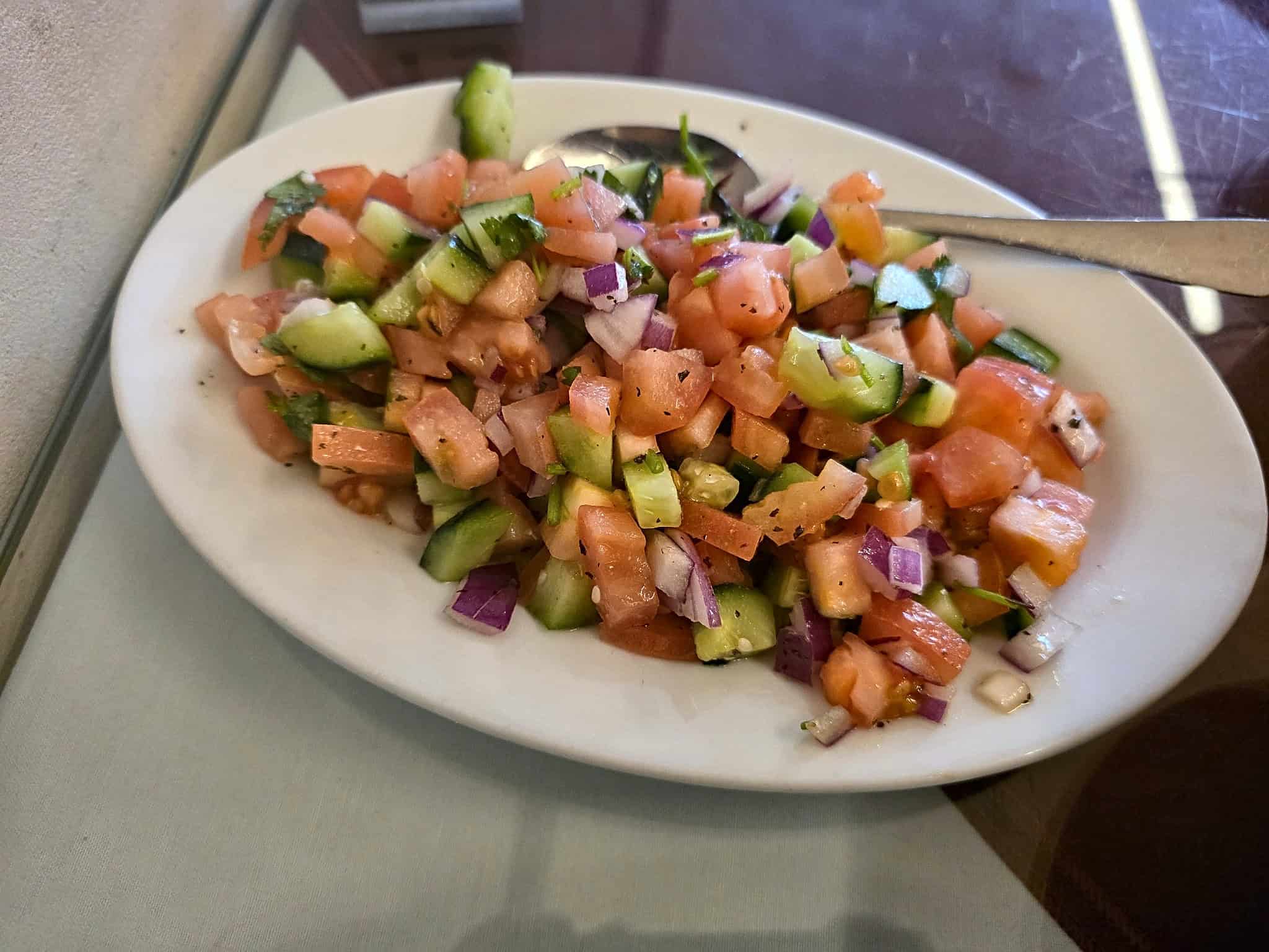 Oval plate of fresh chopped Afghan salad with diced cucumber, tomatoes, red onions, and herbs
